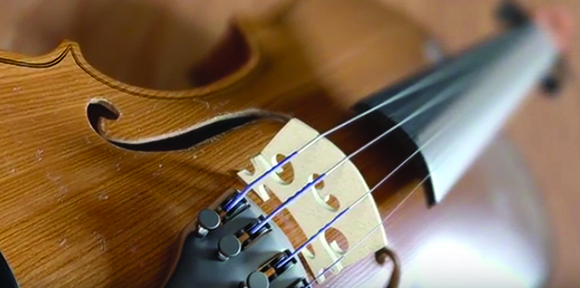 Close-up view of the wooden body, f-hole, and strings of a violin.