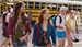 A group of diverse students walking outdoors with backpacks near a yellow school bus.