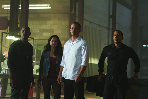 Four people stand together in a dark, warehouse-like setting under dim lighting.
