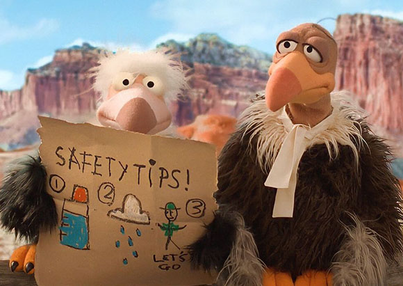Two puppet vultures hold a cardboard sign that says 'SAFETY TIPS!' against a desert canyon background.