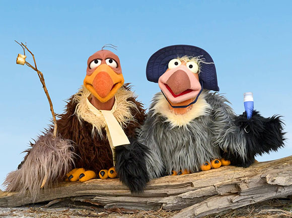 Two fuzzy puppet birds sitting on a weathered log against a clear blue sky.