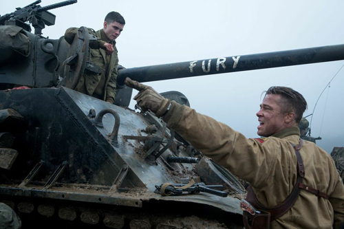 A soldier in tan fatigues points toward a man in a tank turret next to a cannon labeled FURY.