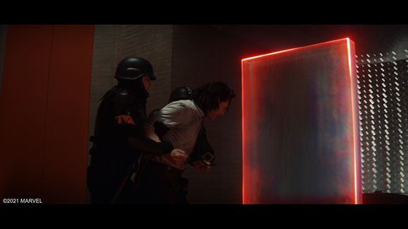 A person in a white shirt is held by two figures in dark tactical gear next to a glowing red rectangular portal.