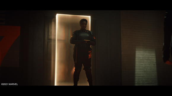 A person in dark tactical gear stands in a glowing doorway against a dark background.