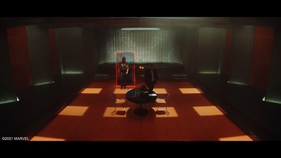 A person stands in a red glowing frame in a dark, modern room with a circular table and two chairs.