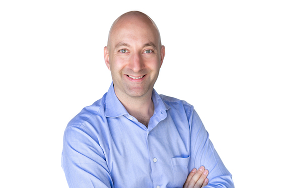 A smiling bald man wearing a light blue button-down shirt against a white background.