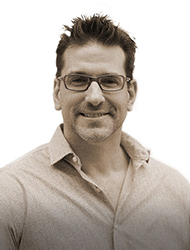 A smiling man with short dark hair and glasses wearing a light-colored button-down shirt.
