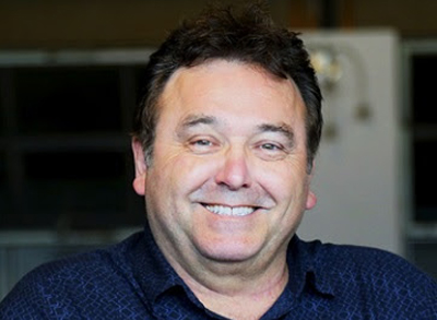A middle-aged man with dark hair smiling at the camera.