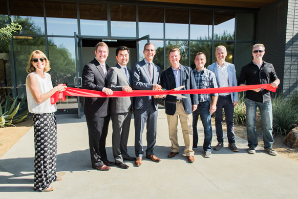 A group of people standing in a line holding a long red ribbon during a ribbon-cutting ceremony.