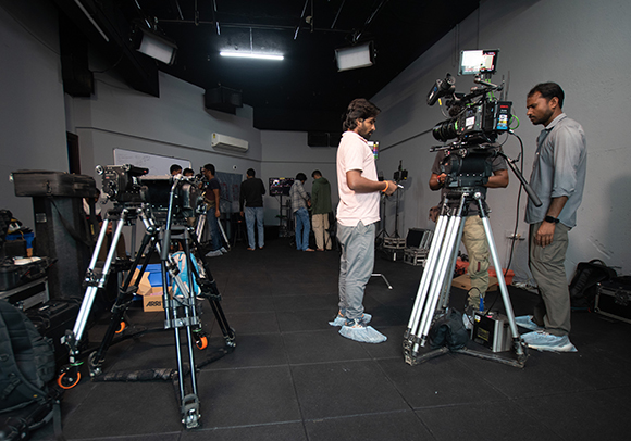 Film crew members operating professional cameras on tripods in a dark studio.