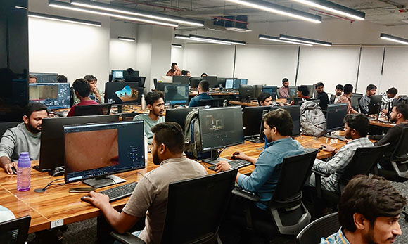 People sitting at desks with computer monitors in a brightly lit, modern office space.