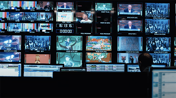 A wall of multiple video monitors displaying various news programs, graphics, and studio footage.