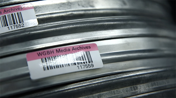 Close-up of metal film reels with pink and white WGBH Media Archives labels and barcodes.