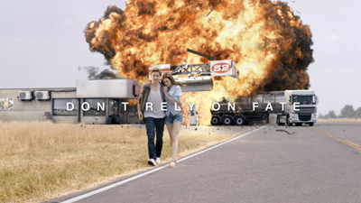 A man and woman walk along a road as a large fireball explosion erupts behind them.