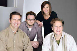 Four smiling adults posing together in a studio setting.