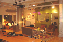 An open-plan office space with wooden desks, a lounge area with armchairs, and warm ambient lighting.