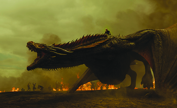 A massive dark dragon flies low over a landscape filled with fire and small figures.