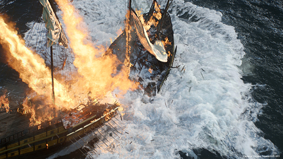 A wooden sailing ship burning intensely amidst white ocean waves.