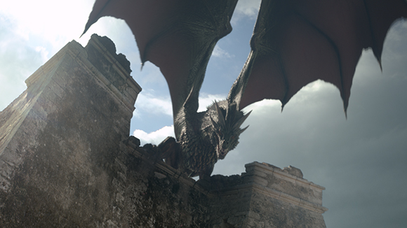 A large dragon with dark scales and expansive wings perched on a weathered stone wall against a cloudy sky.