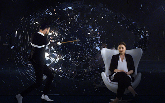 A man in a tuxedo swings a mallet at a dark vortex of shards while a woman sits in a white chair nearby.