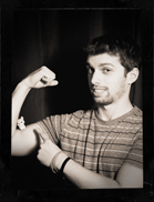 Sepia portrait of a man flexing his bicep and pointing to it with his other hand.