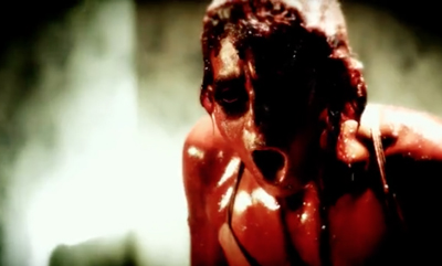 A person with dark, smeared markings on their face and an open mouth, looking distressed.