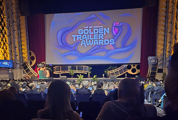 A large screen displays the 26th Annual Golden Trailer Awards logo above a stage and an audience in a theater.