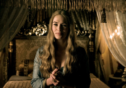 A blonde woman with long wavy hair stands in a dimly lit room in front of an ornate canopy bed.