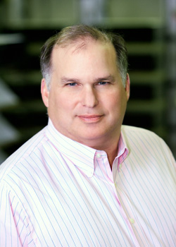 A man with light skin and short brown hair wearing a pink and white striped button-down shirt.