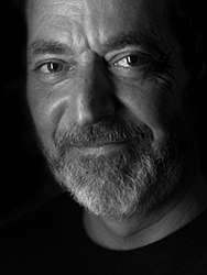 Black and white close-up portrait of a man with a beard and light-colored eyes looking at the camera.