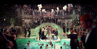 A large group of people in formal attire dancing and swimming around a lit circular pool at night.