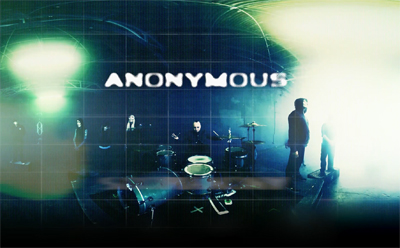 A musical band performs on a dark stage under bright, hazy lights with the word ANONYMOUS in large text.