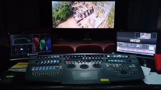 A video editing workstation featuring a large control panel and three computer monitors in a dark room.