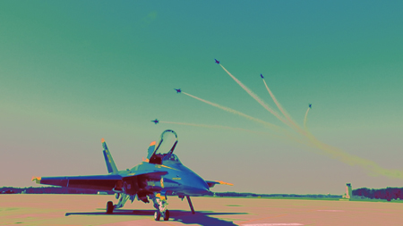 A fighter jet sits on a runway while several planes fly overhead leaving white smoke trails.