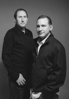 Black and white studio portrait of two men standing side by side against a plain background.