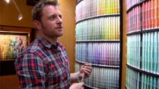 A man in a red and blue plaid shirt looks at rows of colorful cylindrical samples on a shelf.