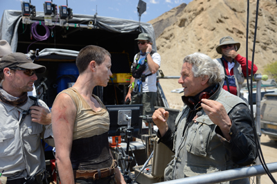 A film director talks to an actress on a desert movie set with crew members in the background.