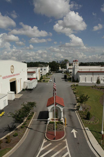 Aerial view of white commercial buildings and a paved road with an American flag in the center.