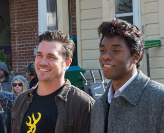 Two men smiling while standing outdoors in front of a brick building.