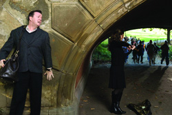A man in a dark suit leans against a stone archway, looking toward a woman standing in a tunnel.