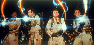 Four men in tan jumpsuits holding glowing proton packs against a dark background with lightning.