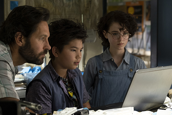 Three young people looking closely at a laptop screen in a dimly lit room.