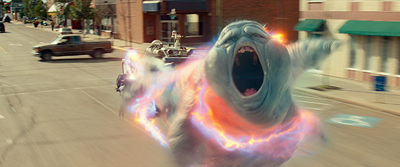 A large, blue, translucent ghost-like creature with an open mouth rushes down a city street.