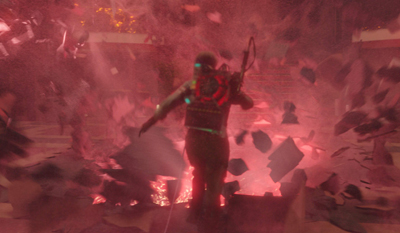 A person with a glowing backpack stands in a red, smoky environment filled with flying debris.