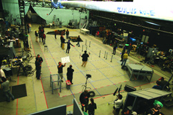 High-angle view of a large film studio set with crew members, lighting equipment, and floor markings.