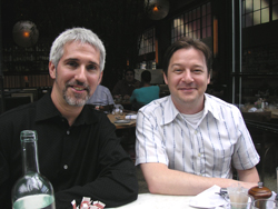 Two men smiling while sitting at a table in a restaurant setting.