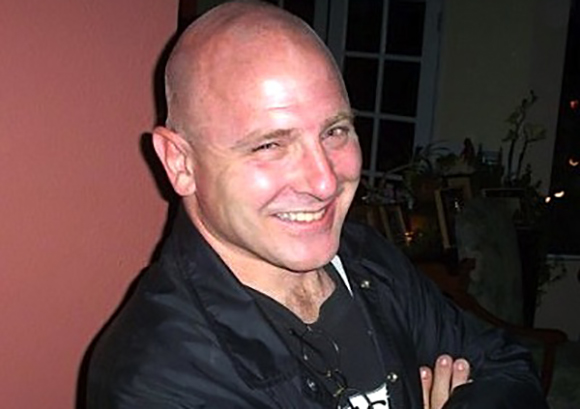 A smiling bald man wearing a black jacket and a black t-shirt.