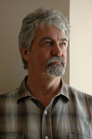 A man with wavy gray hair and a gray goatee wearing a plaid shirt looking toward the light.