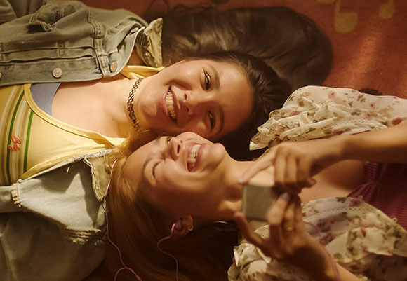 Two smiling young women lying on the floor, one holding a smartphone.