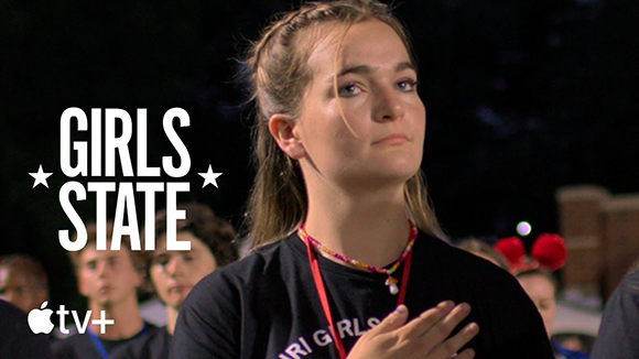 A young woman looks upward with her hand over her heart against a dark background with 'GIRLS STATE' text.